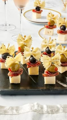 small appetizers with olives and cheese are on a black tray next to wine glasses