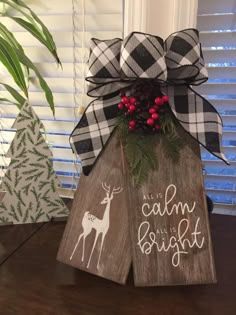 a wooden sign that says calm is bright with a deer and pine cone on top