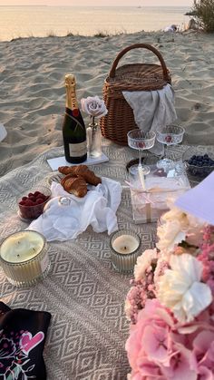 the table is set up on the beach for an outdoor picnic with flowers and champagne