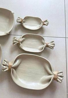 four white dishes with handles and bows on the handles are sitting on a tile floor