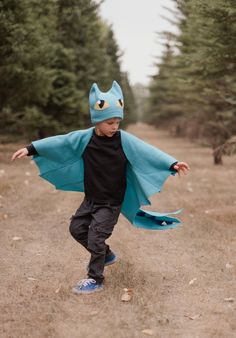 a young boy wearing a blue cape and black t - shirt is running through the woods