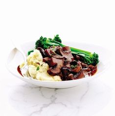 a white bowl filled with meat and broccoli on top of a marble counter