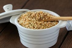 a wooden spoon in a white bowl filled with granola on top of a table