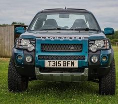 the front end of a blue land rover parked on top of a lush green field