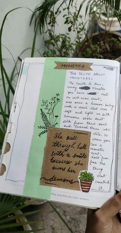 a person holding up a book with writing on it and plants in the back ground