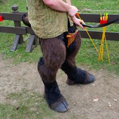 a man dressed up like a gorilla holding a bow and arrow in one hand while standing next to a wooden fence