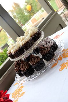 cupcakes are stacked on top of each other on a glass stand in front of a window