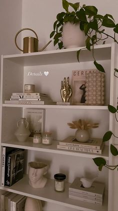 a white book shelf with books and plants on it, along with other decorative items