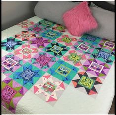 a bed with a quilt on top of it and a pink pillow next to it