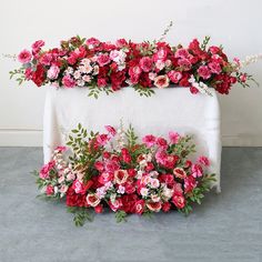 a table topped with lots of pink and red flowers on top of a white cloth