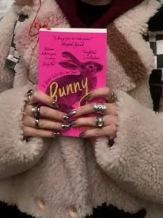 a woman holding up a pink bunny book in front of her face while wearing rings