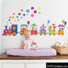 a baby sitting on top of a bed in front of a wall with colorful train decals