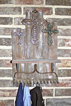 an old wooden cross hanging on a brick wall next to a coat rack filled with clothes