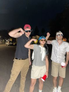 three people posing for the camera with their arms in the air and one person wearing sun glasses