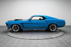 a blue mustang muscle car sitting on top of a round table in a room with white walls