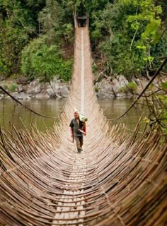 a man walking across a wooden bridge over water