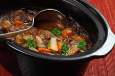 a pot filled with meat and vegetables on top of a wooden table next to a spoon