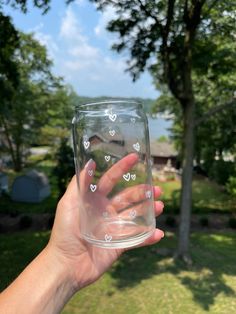 a hand holding up a glass with hearts on it in front of a house and trees