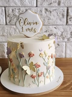 a white cake with flowers and butterflies on it sitting on top of a wooden table