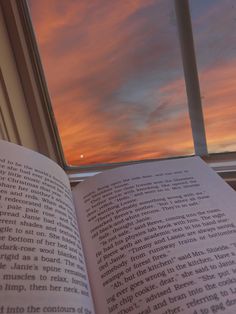 an open book sitting on top of a window sill in front of a sunset