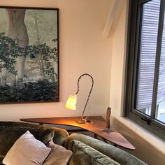 a living room with a couch, lamp and painting on the wall above it in front of a window