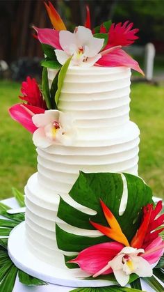 a three tiered cake with flowers and leaves on the top is decorated in white frosting