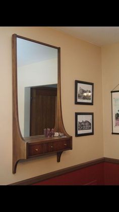 a large mirror hanging on the wall above a wooden shelf with pictures and other items