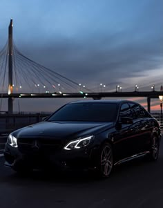 a black car parked in front of a bridge at night with the sun setting behind it