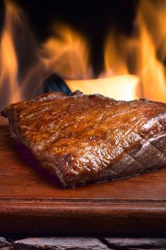 a steak on a cutting board with a knife next to it and flames in the background