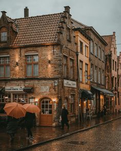 people walking down the street with umbrellas on a rainy day in an old european town