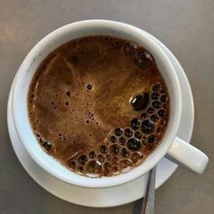 there is a cup of coffee on the saucer with spoons next to it