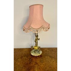 a lamp that is sitting on top of a wooden table with a pink shade over it