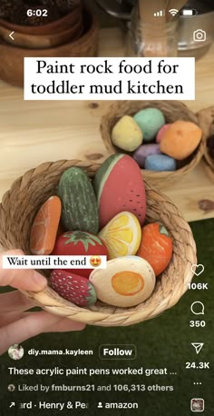 a person holding a basket full of fake food in front of a screen with the words paint rock food for toddlers mud kitchen