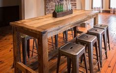 a wooden table with four stools in front of it and a brick wall behind it