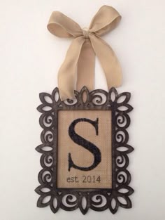 an ornate frame with the letter s on it and a ribbon hanging from the side