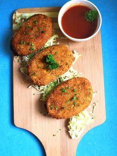 three crab cakes with coleslaw and sauce on a cutting board