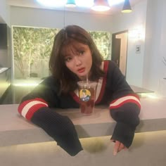 a woman leaning on a counter with a drink in her hand and pointing at the camera