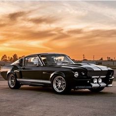 an old black mustang sitting in the middle of a parking lot at sunset or dawn