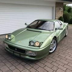 a green sports car is parked in front of a garage with a white door and brick driveway