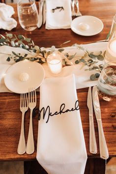 a place setting with napkins, candles and silverware on a wooden dining table