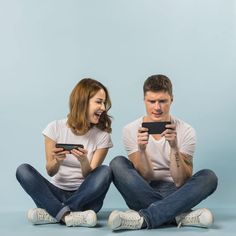 two people sitting on the floor with their cell phones in front of them, laughing