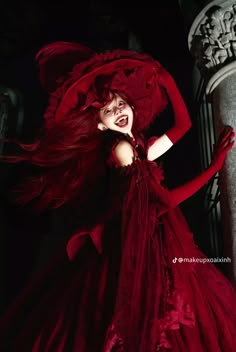 a woman in a red dress and hat posing for the camera with her hair blowing