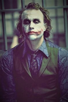 a man dressed as the joker sitting in front of a jail cell