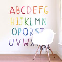 a white chair sitting in front of a wall with letters painted on it and a window