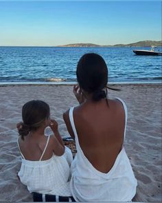 two women sitting on the beach looking out at the water