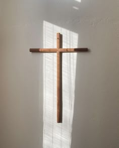 a wooden cross hanging from the side of a white wall with sunlight coming through it