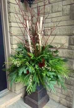 a vase filled with greenery and candles on top of a stone floor next to a brick wall