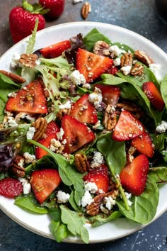 a salad with spinach, strawberries and pecans in it on a plate