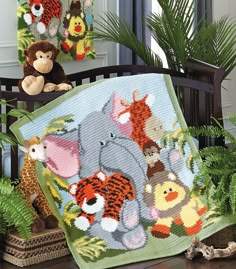 a crocheted baby blanket with animals on it next to plants and stuffed animals