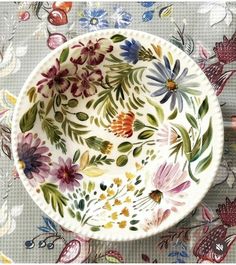 a bowl with flowers painted on it sitting on top of a tablecloth covered surface